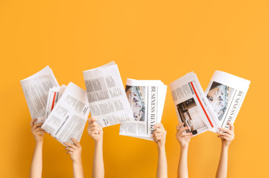 新聞を持つ女性の手とオレンジの背景